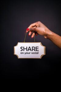 Une main tient une pancarte sur laquelle est écrit « Partager sur vos réseaux sociaux » sur un fond sombre.