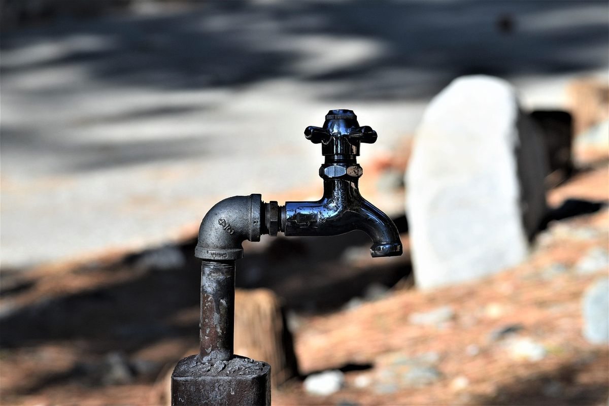 Pompe à eau noire sur un socle, pomme de douche, rochers, végétation, soleil Pompe à eau noire sur un socle, pomme de douche, rochers, végétation, soleil
