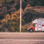 Camper blanc et rouge stationné sur le bord de la route, près de buissons et d'un mât de ligne