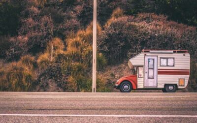 Camper blanc et rouge stationné sur le bord de la route, près de buissons et d'un mât de ligne