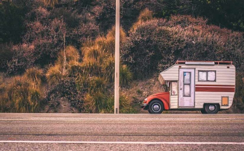 Camper blanc et rouge stationné sur le bord de la route, près de buissons et d'un mât de ligne