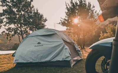 Tente de camping blanche près d'un lac, soleil couchant, moto à l'avant-plan