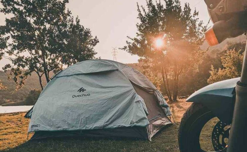 Tente de camping blanche près d'un lac, soleil couchant, moto à l'avant-plan