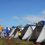 Des tentes bleues et des personnes sur un terrain herbeux