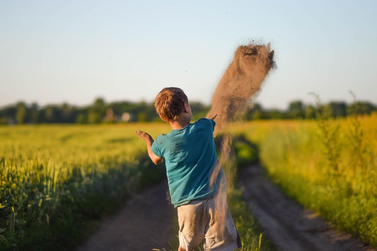 Enfant lançant de la terre dans un champ au coucher du soleil Enfant lançant de la terre dans un champ au coucher du soleil