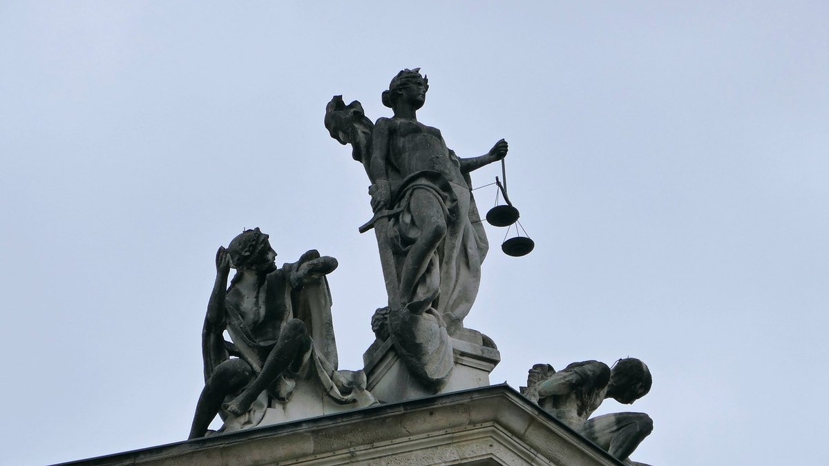 Statue de la Justice tenant une balance, avec figures allégoriques et ciel bleu Statue de la Justice tenant une balance, avec figures allégoriques et ciel bleu
