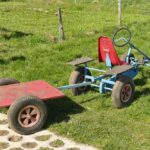 Un go-kart bleu avec remorque rouge sur gazon à côté d'un trottoir
