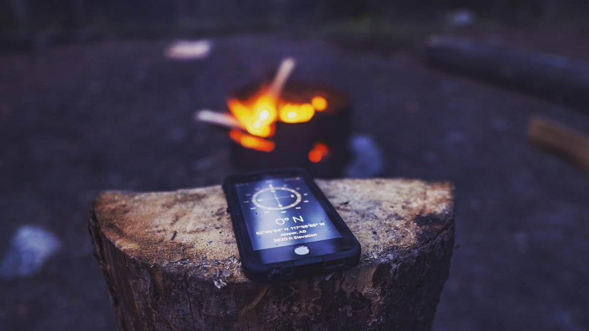 Un smartphone sur un tronc d'arbre montre une boussole près d'un feu de camp