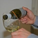 Une main verse du vin blanc dans un verre à vin