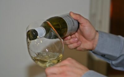 Une main verse du vin blanc dans un verre à vin