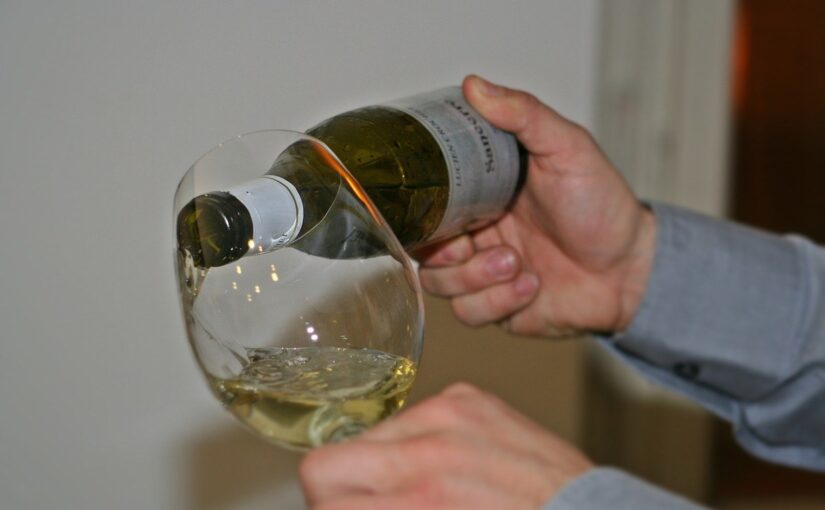 Une main verse du vin blanc dans un verre à vin
